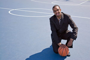Sports psychologist in suit kneeling on a basketball court with a basketball in hand